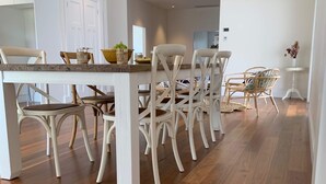Un comedor con una mesa y sillas blancas, suelo de madera y una puerta blanca al fondo.