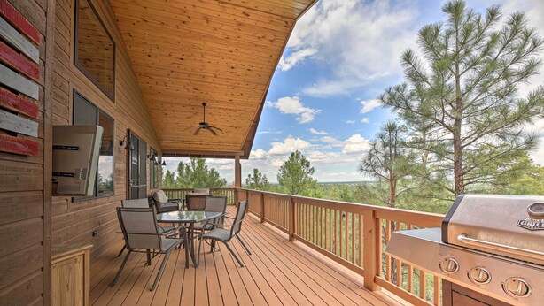 Un terrazzo in legno con barbecue, posti a sedere all'aperto e vista sugli alberi.