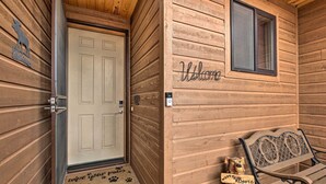 Una baita di legno con una porta bianca, un cartello di benvenuto, una panchina e un cartello con la scritta 'Wizzy Roots'.