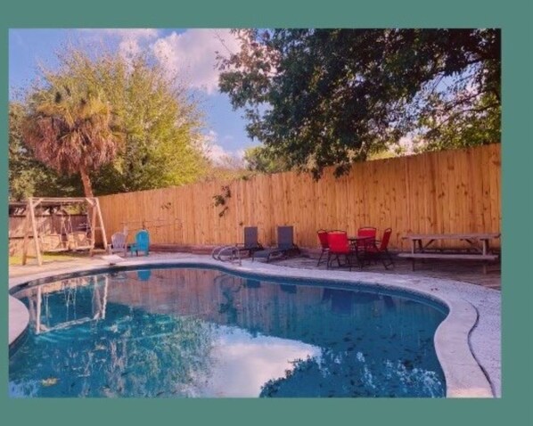 Relax by the pool surrounded by a yard with a wooden fence and a swing set.