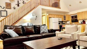 A living room with a brown leather sofa, a wooden coffee table, and a staircase leading to an upper level. - Spacious Cabin Right Next to Cacapon State Park (Berkeley Springs)