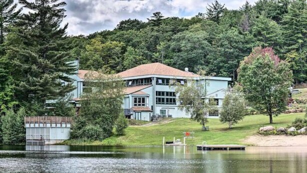 A large, light blue building with a red roof, surrounded by trees and a lake. - Spacious Home in Waterville Estates close to the community center (Campton)