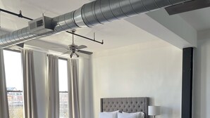 Une chambre d’hôtel moderne dotée d’un grand lit, d’un ventilateur de plafond, d’une table à manger avec des chaises et offrant une vue sur l’extérieur.