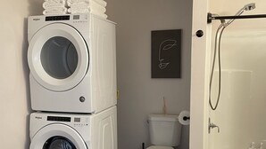 Une buanderie équipée d’une machine à laver et d’un sèche-linge superposés, de toilettes et d’une baignoire avec un rideau de douche.
