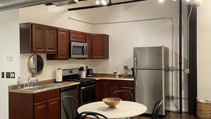 Une cuisine moderne avec des meubles en bois, des appareils électroménagers en acier inoxydable et un coin repas comprenant une table ronde et des chaises.