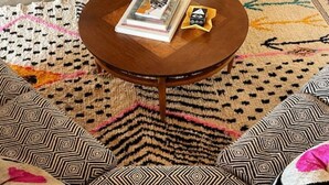 A room with a patterned floor, a round wooden table with a book and a small object on it, and two patterned cushions. - Spacious, Stylish “Niji Suite” @ La Dea (Santa Fe)