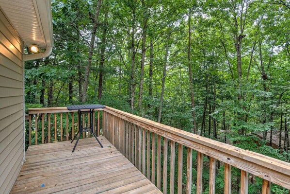 Una terraza de madera con una mesa y sillas, rodeada de un bosque frondoso.