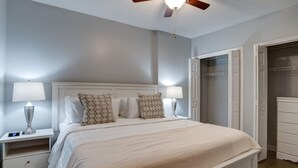 A bedroom with a large bed, two bedside tables with lamps, a ceiling fan, and a walk-in closet.