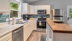 A modern kitchen with white cabinets, stainless steel appliances, and a wooden countertop.