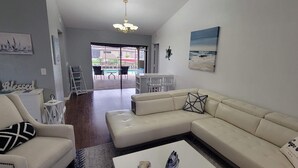 Ein Wohnzimmer mit einem beigen Sofa, einem weißen Sessel und einem Couchtisch. An der Wand hängt ein Gemälde und ein Schild mit der Aufschrift 'STAY anchored.'