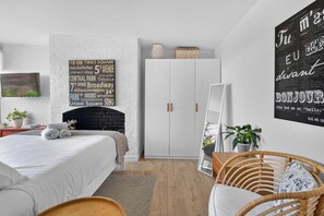 A modern bedroom with a white brick wall, a bed with white bedding, a white wardrobe, a blackboard with street names, and a 'BONJOUR' sign. - Stylish Studio in Heart of Annandale Village (Annandale)