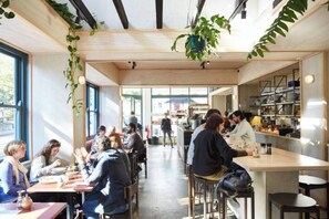 An indoor dining area with wooden tables and chairs, potted plants, and a view through large windows. - Stylish Studio in Heart of Annandale Village (Annandale)