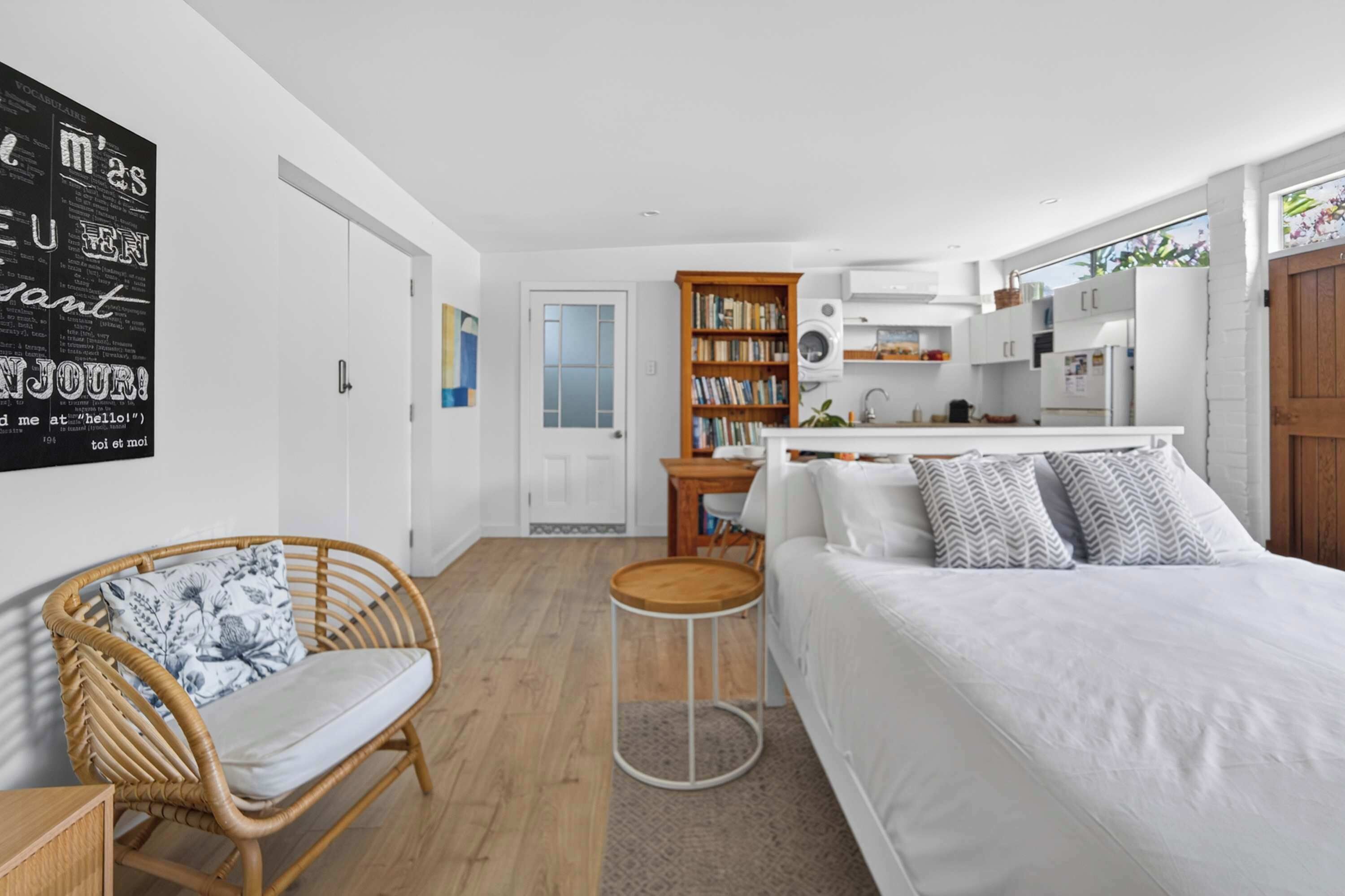 Une chambre moderne avec un grand lit, une petite table ronde, un fauteuil en osier et une bibliothèque.