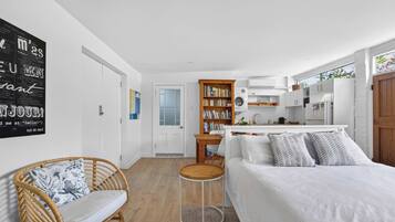 Une chambre moderne avec un grand lit, une petite table ronde, un fauteuil en osier et une bibliothèque.