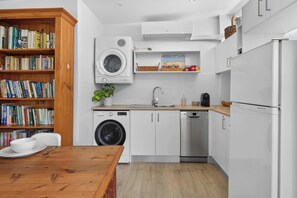 A modern kitchen with a washing machine, dishwasher, and a wooden bookshelf filled with books. - Stylish Studio in Heart of Annandale Village (Annandale)