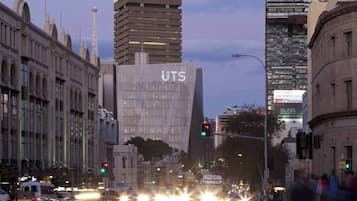 A city street with modern buildings, including a prominent UTS building, traffic lights, and vehicles.