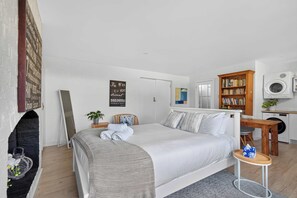A modern bedroom with a large bed, a small bedside table, a bookshelf, a mirror, and a washing machine. - Stylish Studio in Heart of Annandale Village (Annandale)