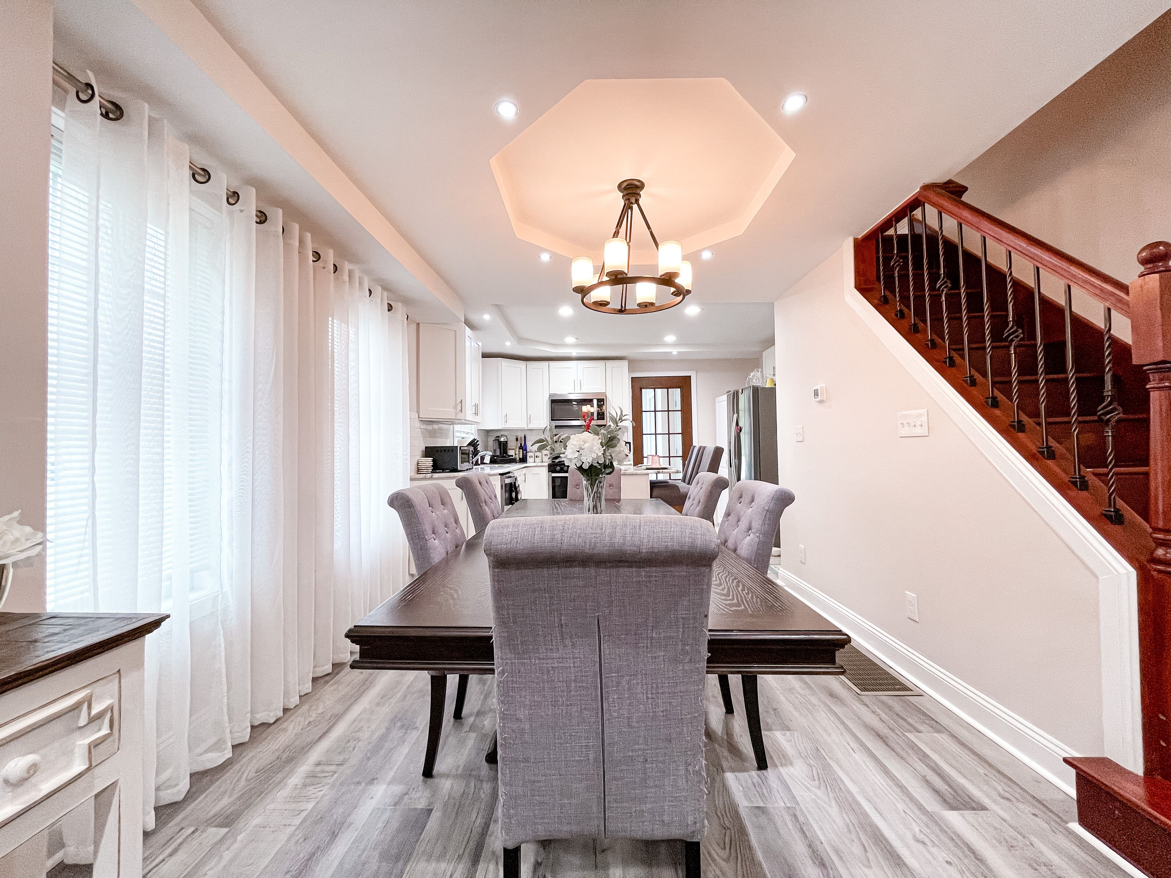 A spacious dining area with a long table, grey upholstered chairs, and a chandelier.
