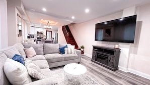 A modern living room with a grey sofa, a white coffee table, and a flat-screen TV mounted on the wall. - Cheerful & Modern Home w/ a Walkout Deck Area (Glenside)