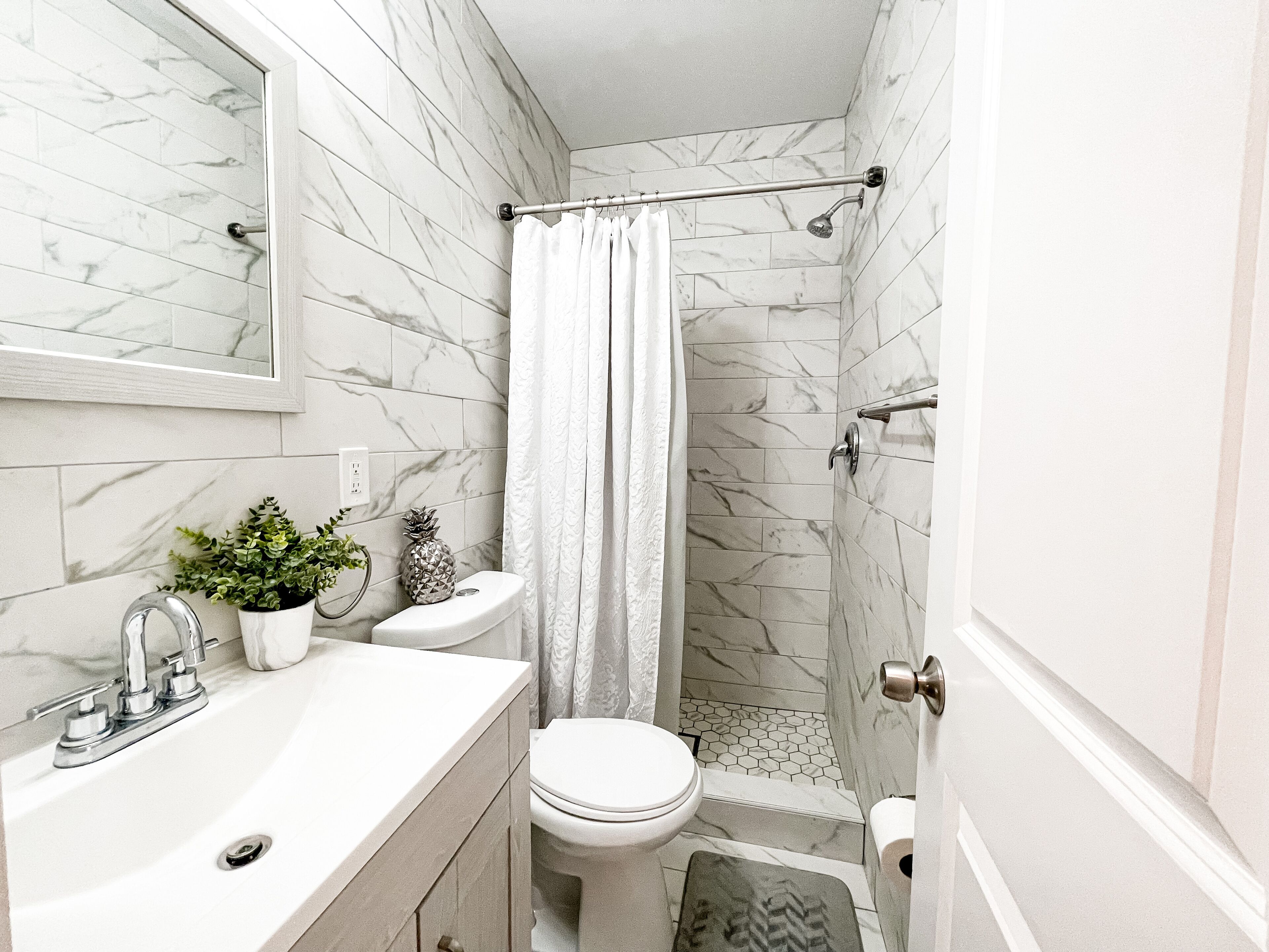 Une salle de bain avec un mur en marbre, un rideau de douche, des toilettes, un lavabo et une plante en pot.