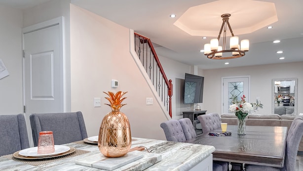 A modern kitchen with a marble countertop, a dining area with a table and chairs, a staircase, and a living area with a sofa and a TV. - Cheerful & Modern Home w/ a Walkout Deck Area (Glenside)