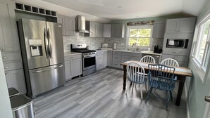 A modern kitchen with stainless steel appliances, grey cabinetry, and a dining area with two chairs.