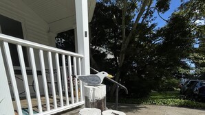 A porch with a white railing, a bird sculpture, and two wooden posts with ropes and a buoy.