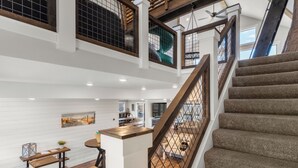 Interior com vários níveis, escada, corrimãos de madeira e área de cozinha.