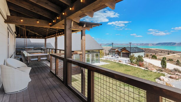 Um deck de madeira com mobiliário externo, uma área coberta com luminárias pendentes e vista para uma paisagem montanhosa.