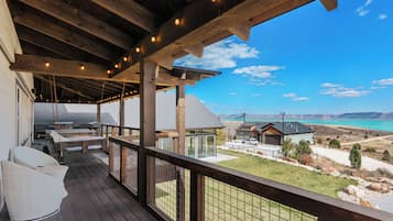 Une terrasse en bois avec des meubles d’extérieur, un espace abrité agrémenté de guirlandes lumineuses, et une vue sur un paysage montagneux.