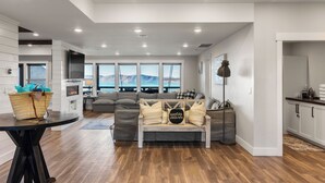 Uma sala de estar moderna com sofá, mesa e vista para montanhas através de grandes janelas.