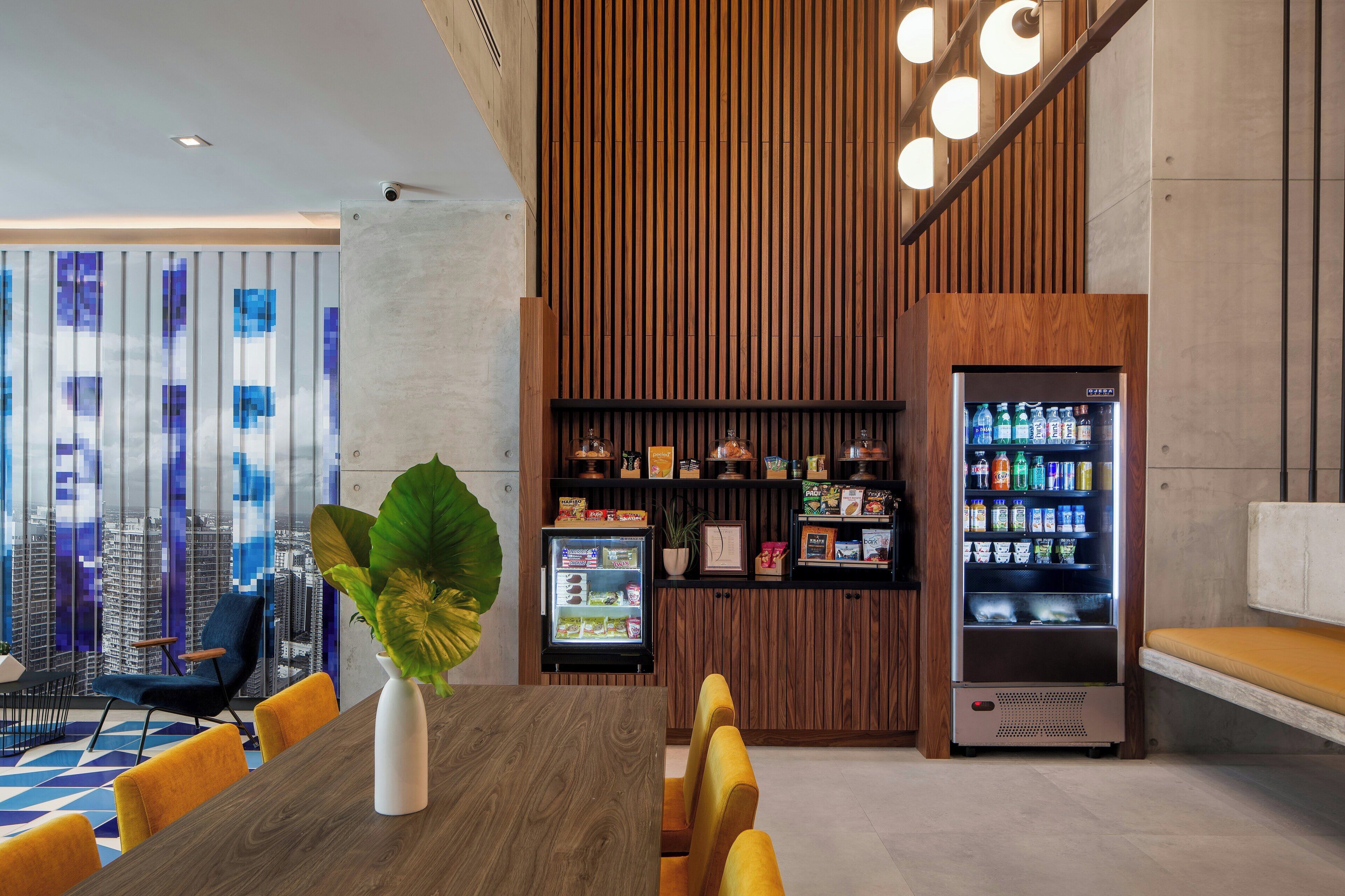 A modern hotel lobby with a dining area, a vending machine, and a view of the cityscape.