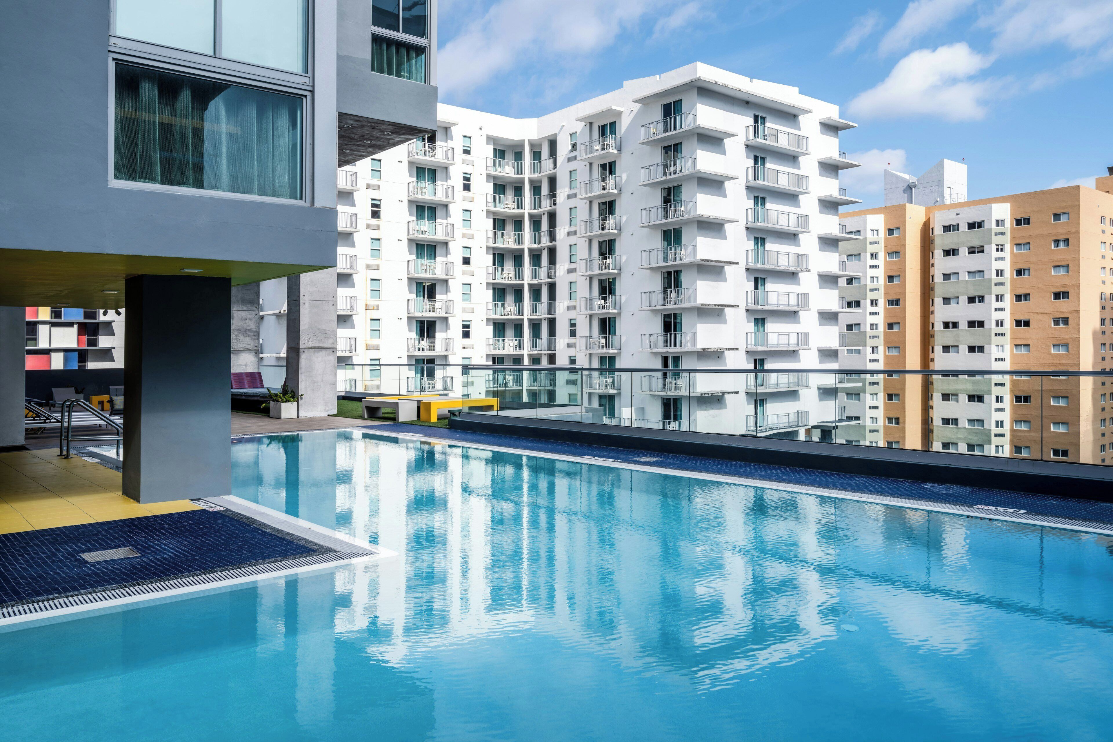A modern building with a swimming pool, balconies, and a clear sky.