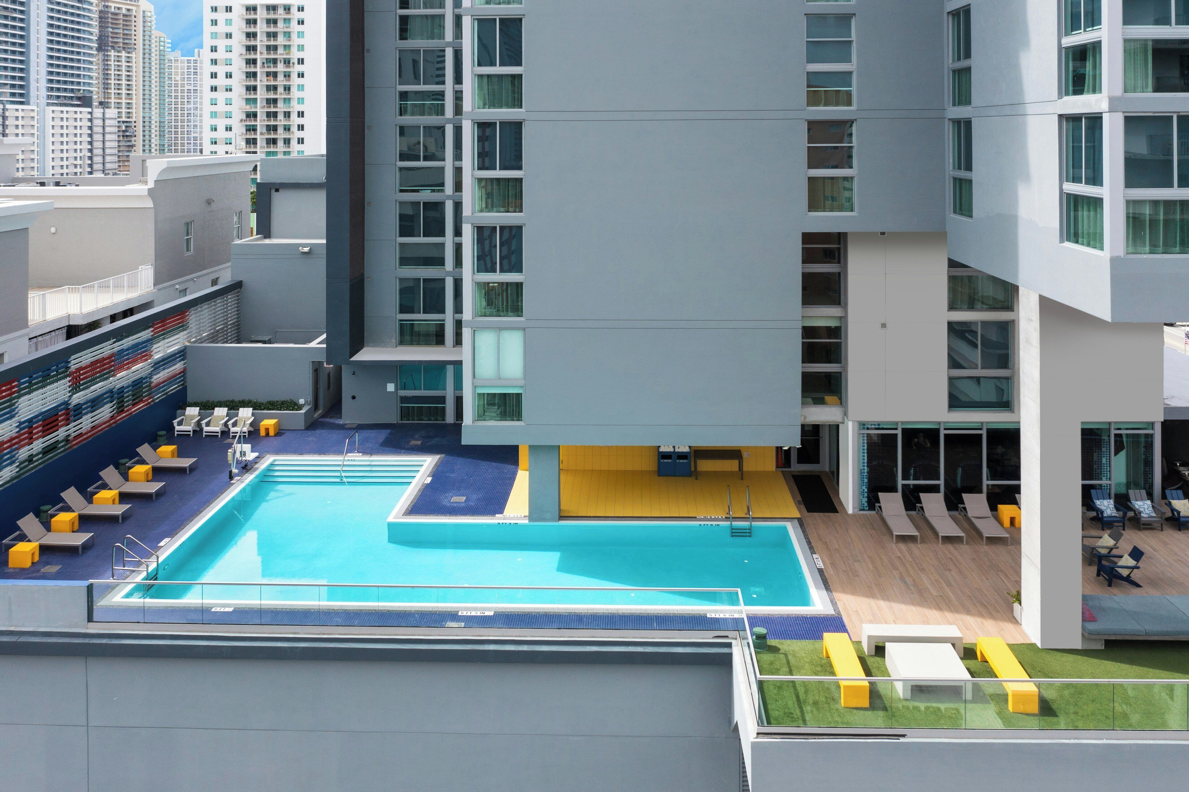 Une piscine sur le toit, dotée de chaises longues et offrant une vue sur les immeubles environnants.