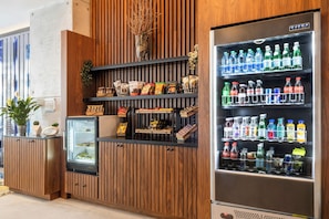 Ein Getränkeautomat mit Getränken und Snacks, ein gekühlter Verkaufsstand und eine Holzwand mit einem Blumentopf.