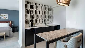 A modern hotel room with a kitchenette, a dining area, and a bed.
