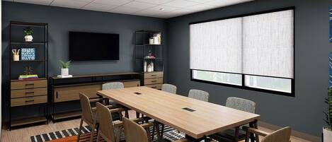 A conference room with a long table, chairs, a TV, shelves with books and plants, and a large window with blinds.