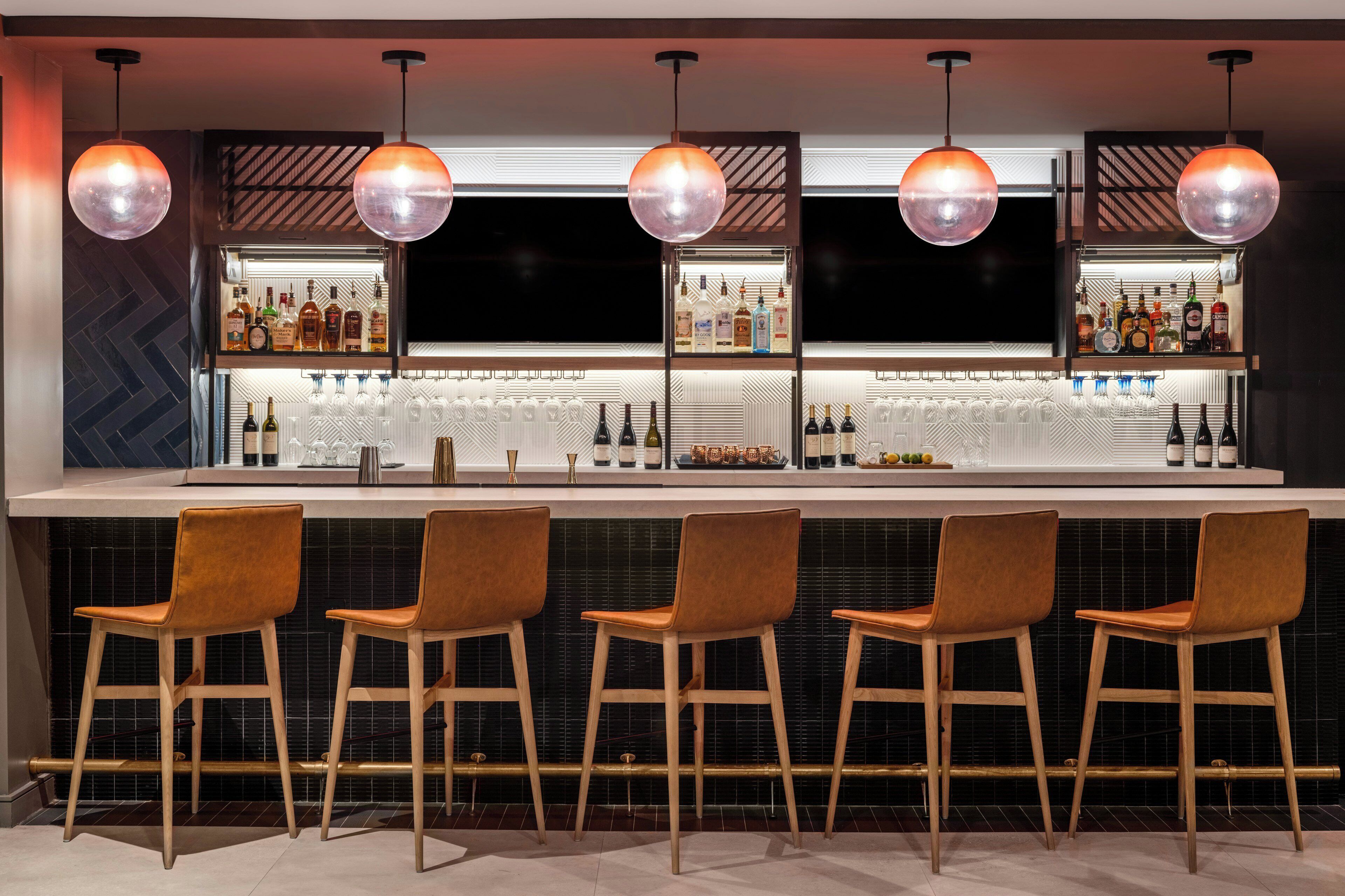 Zona de bar amb un disseny modern, que destaca per una barra llarga, diversos tamborets i il·luminació penjant.
