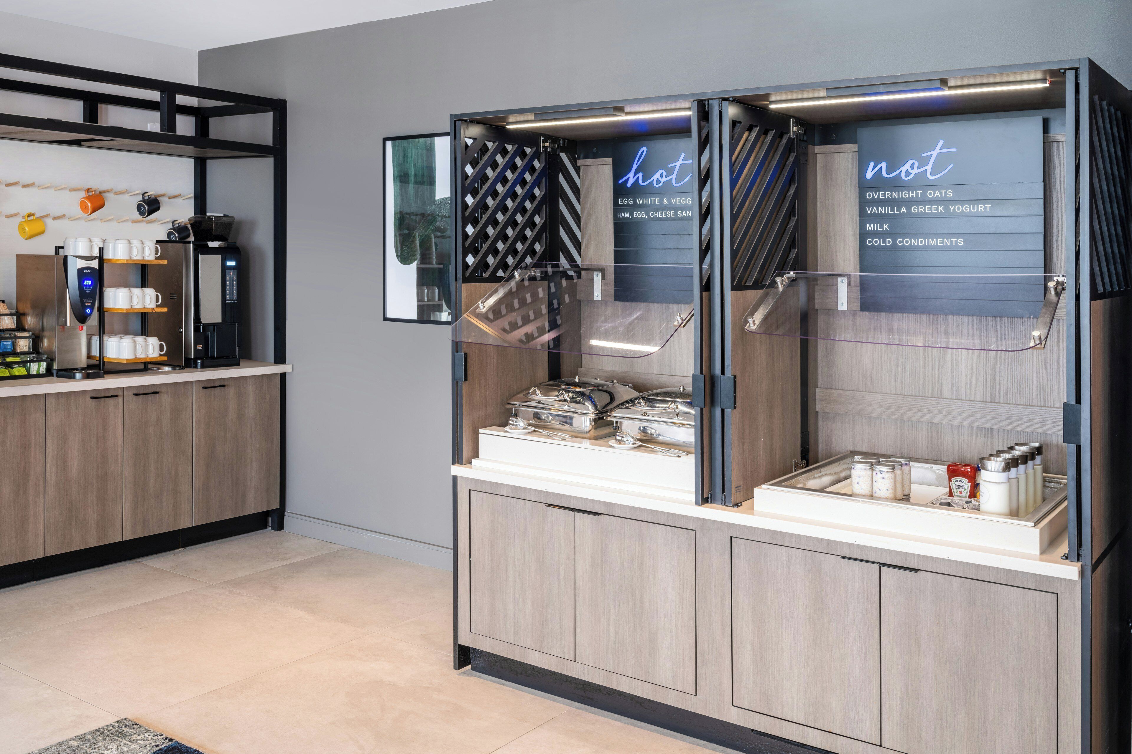 A self-service beverage station with a coffee machine, a selection of condiments, and a menu board.