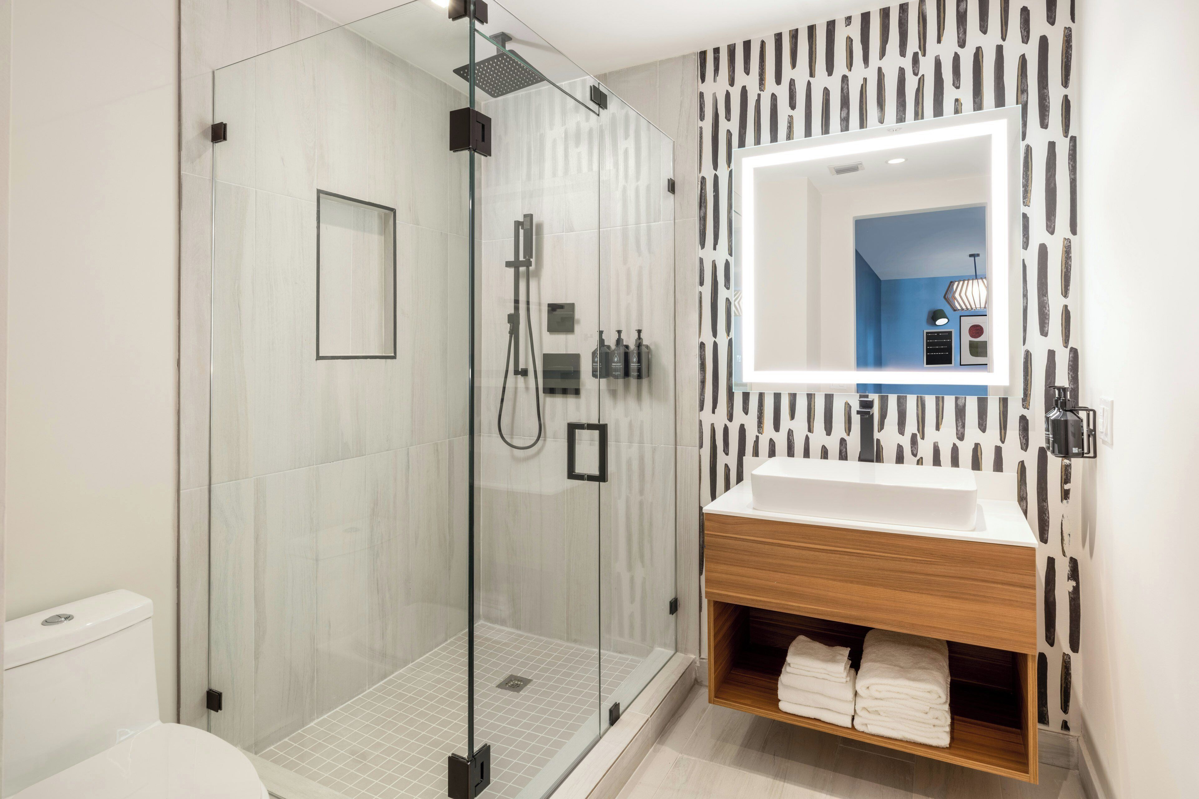 Un baño moderno con ducha envuelta en vidrio, un lavabo blanco y un mueble de tocador de madera.
