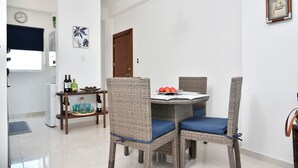 A dining area with wicker chairs and a table set for four, a clock on the wall, and a door leading to another room. - espectacular apartamento (Playa Juan Dolio)