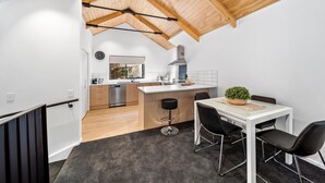 A modern kitchen with wooden beams, a dining area with a table and chairs, and a view into the adjacent living space. - 3 Bedroom Modern Alpine Apartment (Queenstown)