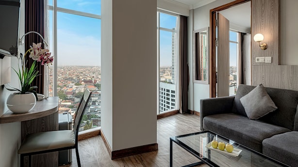 A modern living room with a sofa, a coffee table, and a view of the city through large windows. - GoldVitel Hotel Surabaya (Surabaya)