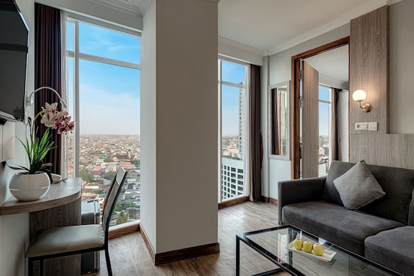 A modern living room with a sofa, a coffee table, and a view of the city through large windows. - GoldVitel Hotel Surabaya (Surabaya)