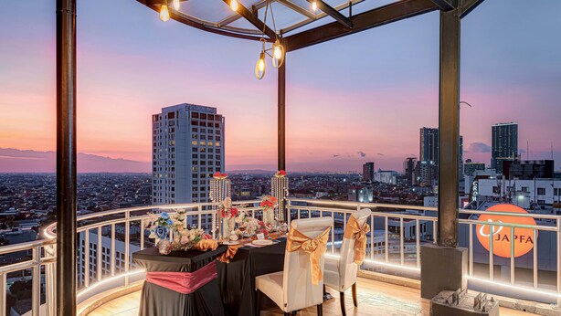 A rooftop dining area with a city view, a table set with flowers, and a 'JAPFA' sign. - GoldVitel Hotel Surabaya (Surabaya)
