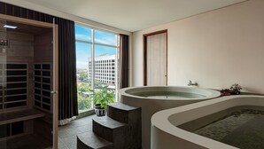 A modern bathroom with a large bathtub, a shower area, and a view of the city. - GoldVitel Hotel Surabaya (Surabaya)