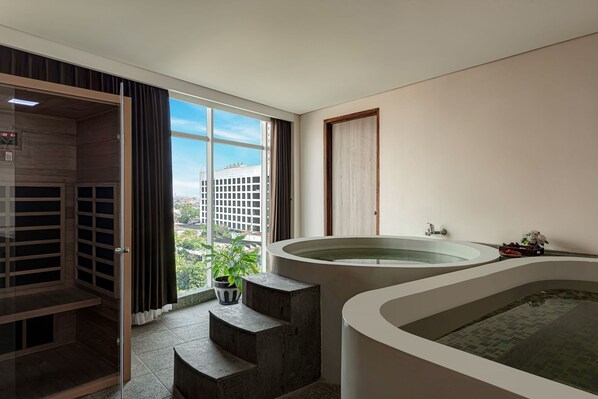 A modern bathroom with a large bathtub, a shower area, and a view of the city. - GoldVitel Hotel Surabaya (Surabaya)