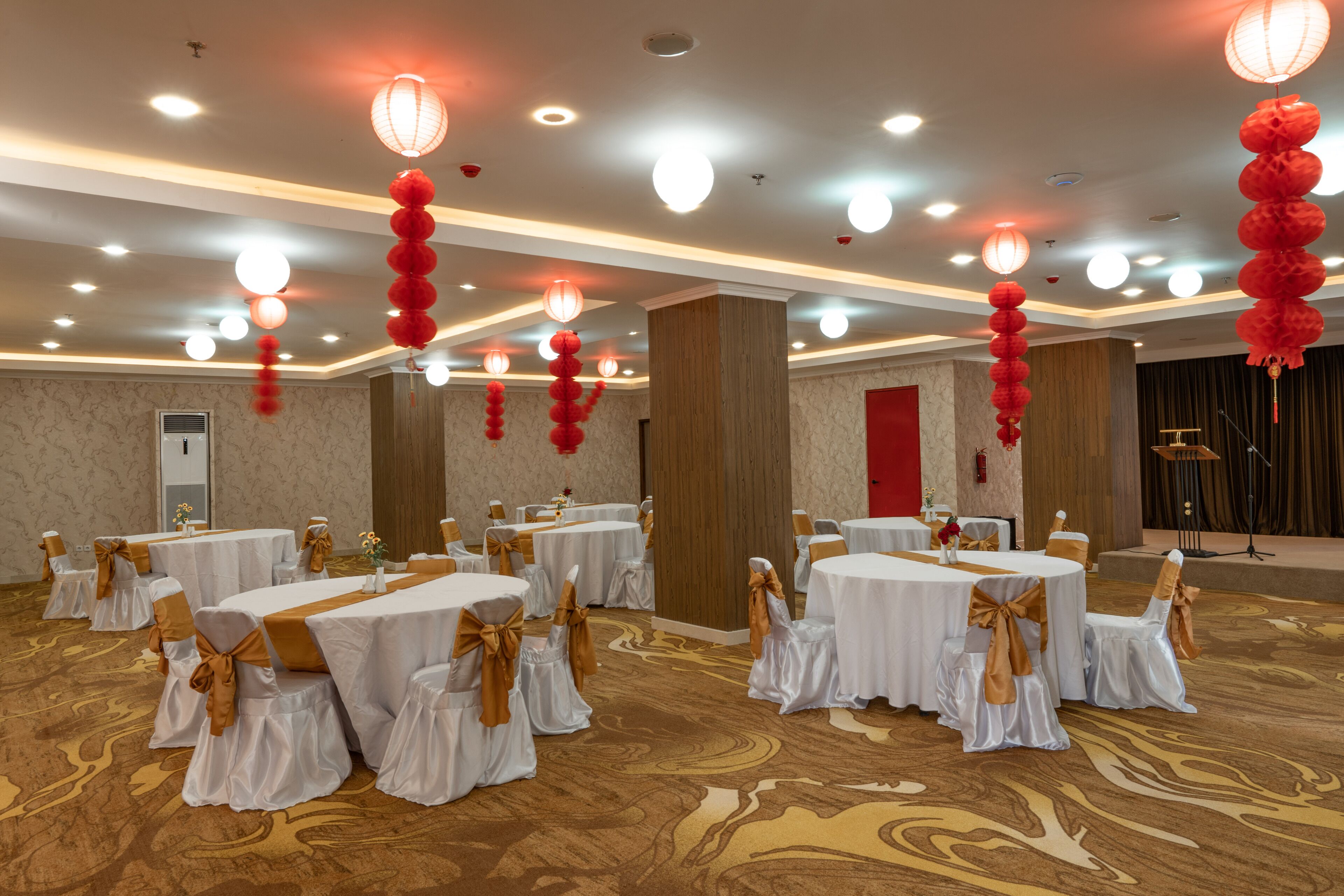 A banquet hall with round tables, chairs, and red lanterns.