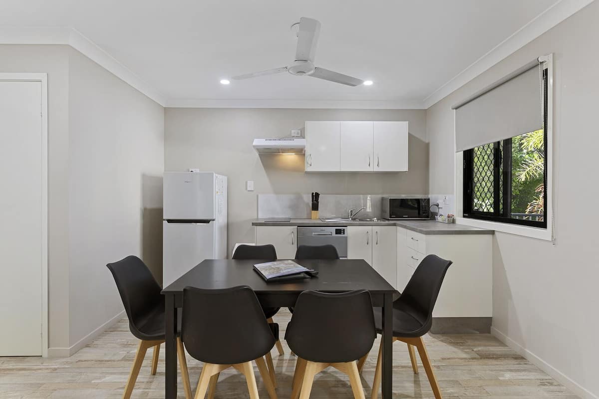 A compact kitchen with white cabinets, a microwave, a refrigerator, and a dining table with four chairs.