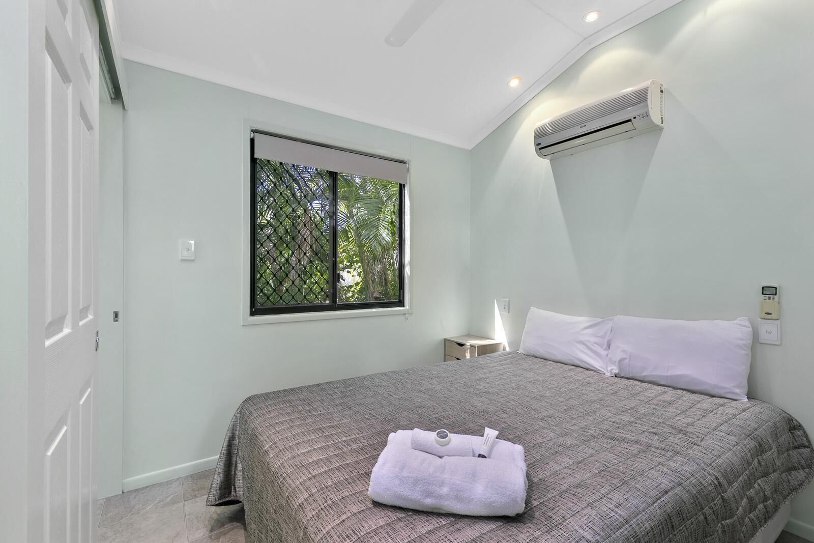 Un dormitorio con cama, ventana con vistas, aire acondicionado y mesita de noche.